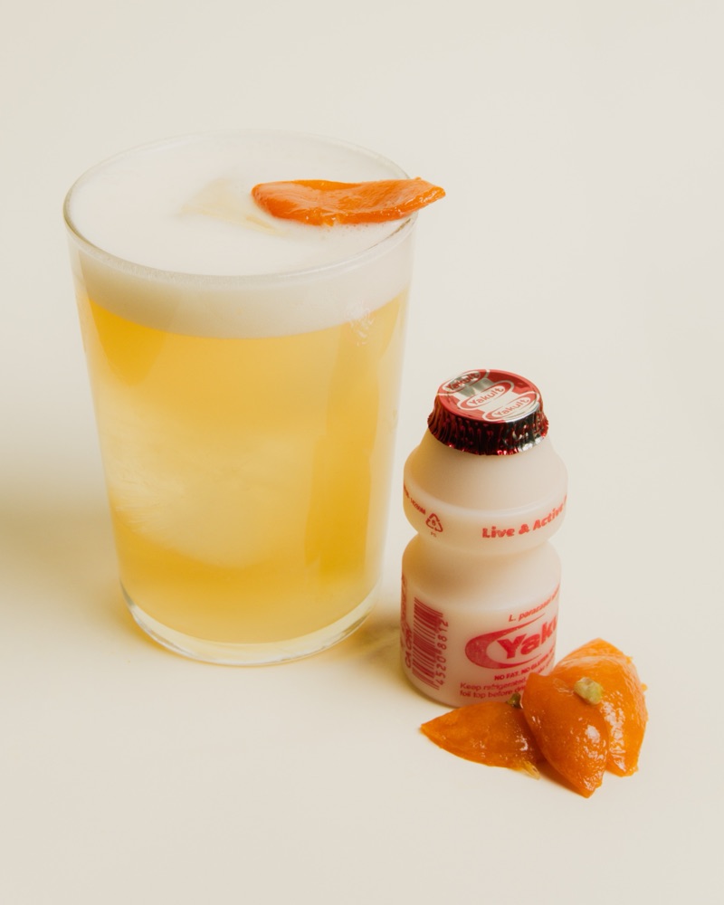Chinito: a golden jasmine calamansi tea with foam and a candied calamansi garnish, next to a Yakult bottle