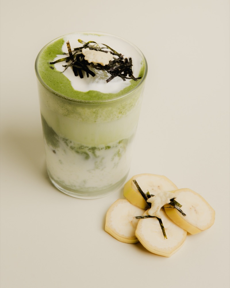 Hagwon Uyu: a layered matcha banana milk in a glass, topped with seaweed and a rice cracker, banana slices alongside