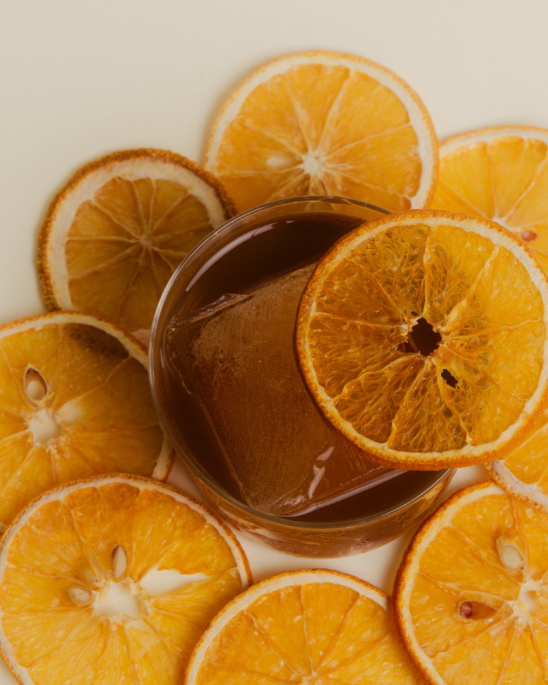 Ổi Kiên: a dark guava espresso milk punch in a rocks glass, ringed with dried orange wheels